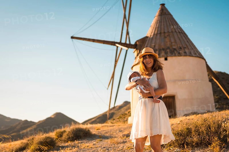 Mother holding a newborn baby next to a windmill in Cabo de Gata, Spain