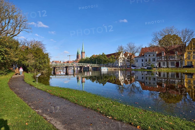 River Trave at high water, general architecture, footpath, pedestrian bridge, trees and bushes, reflections on the water surface, blue sky with fair weather clouds, Hanseatic city of Lübeck, independent city, Schleswig-Holstein, Germany