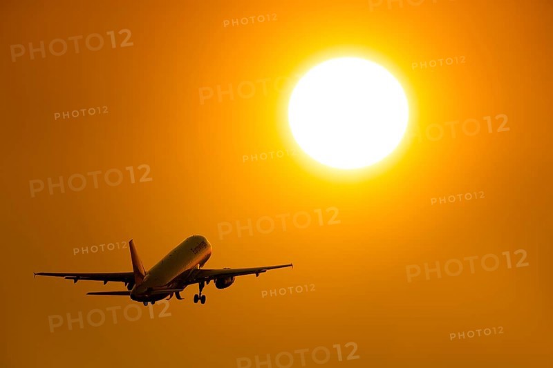 Silhouette of an aircraft taking off in front of a bright orange sunset