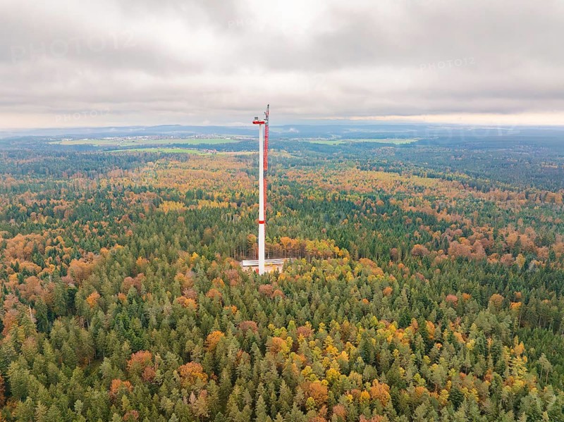 A wind power tower rises above an autumnal forest, shrouded in mist, into a wide landscape, wind farm construction site, Grömbach, Black Forest, Germany