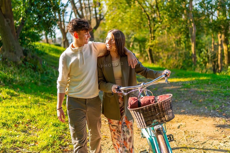 Young couple walking hand in hand through a picturesque park, riding a bicycle and basking in the warm glow of golden hour sunlight