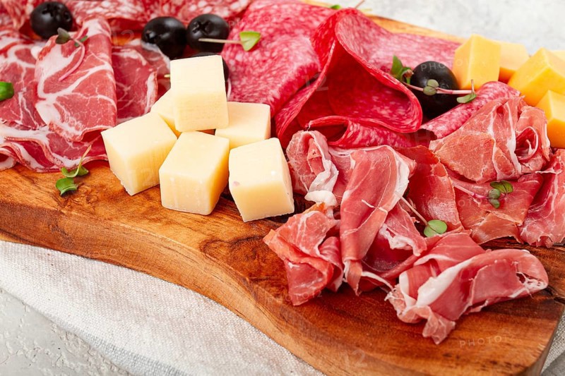 Assorted, sliced meat appetizer, prosciutto, salami and ham, with cheese and olives, on a wooden board, breakfast, top view, close-up, no people