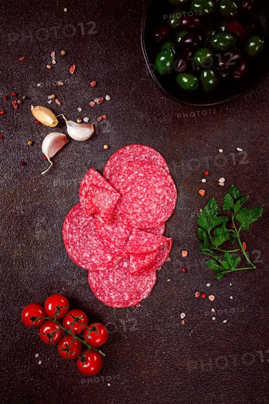 Composition of sliced salami, with fresh tomatoes, garlic and green olives, on a dark surface, appetizer, no people