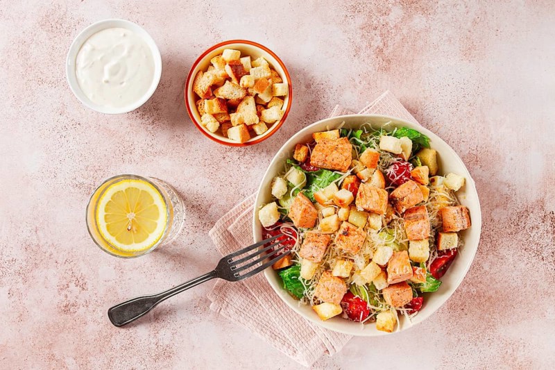 Caesar salad with salmon, with croutons and dressing, in a salad bowl, on a pink table