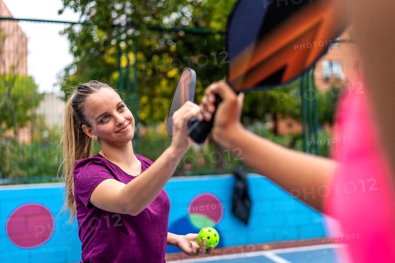 Smiling sportive blonde woman shaking racket with partner in a pickelball court
