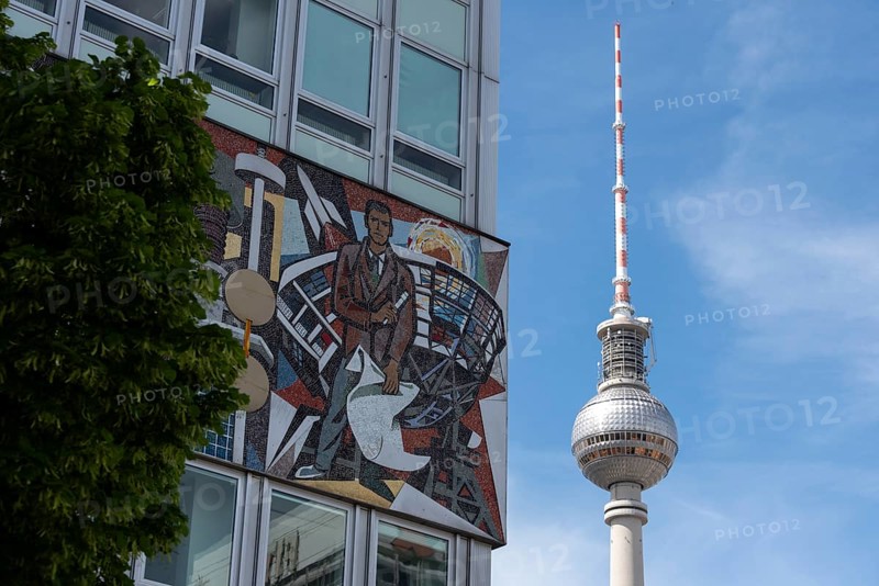 Television tower and building with wall mosaic and tree in front of blue sky, combination of art and architecture, Berlin, Germany