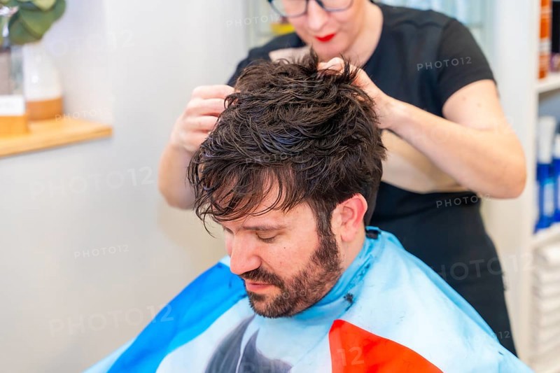 Hairstylist attaching a new capillary prosthesis to a man's head sitting on a salon