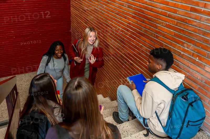 Multi ethnic students walking down the stairs and greeting a classmate sitting on the steps