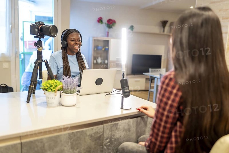 Two young women recording a podcast using laptop, microphone and camera in their home studio