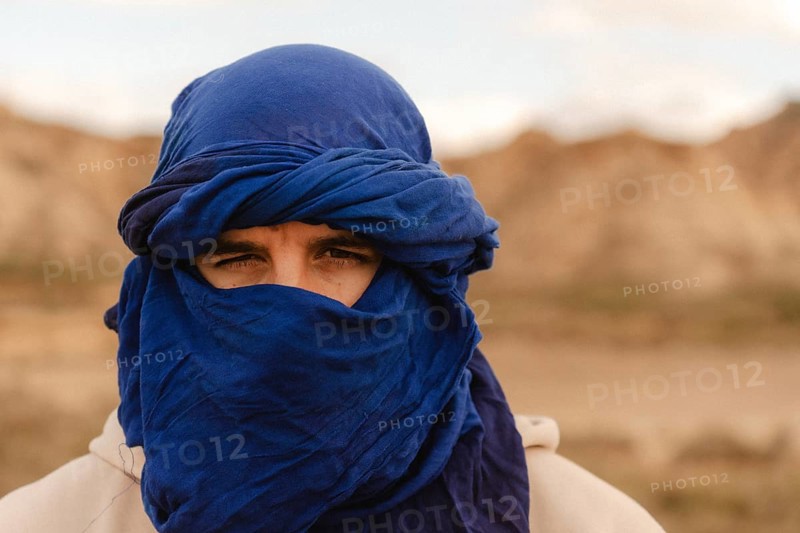 Portrait of a tuareg man adorned in an indigo tagelmust, set against the vast, arid landscape of the sahara desert