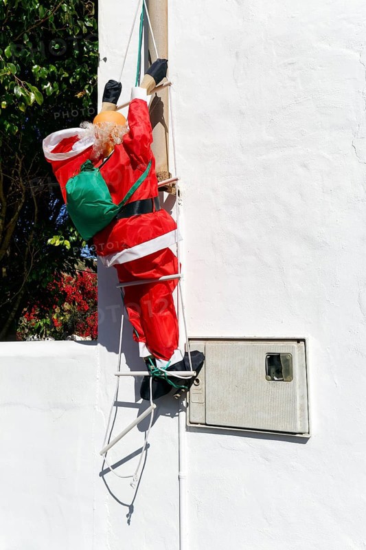 Artificial Father Christmas with rucksack, climbs up ladder, white house facade, funny decoration, Haria, Lanzarote, Canary Islands, Spain