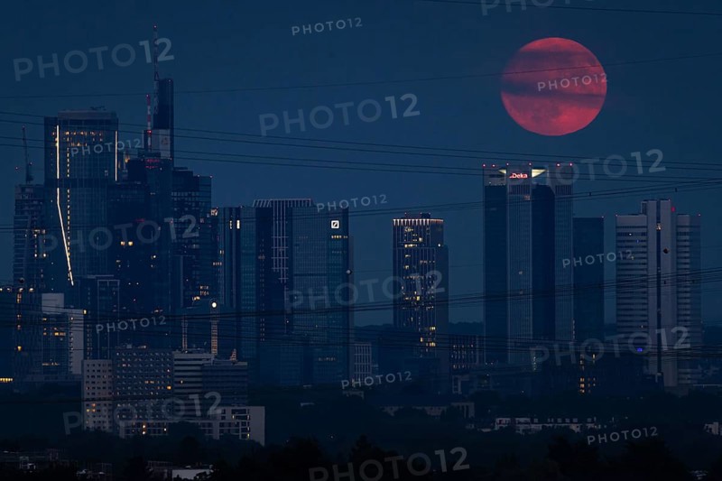 The red full moon passes over Frankfurt's banking skyline. Because of its reddish colour when it rises, the full moon in July is also known as the strawberry moon or blood moon, Frankfurt am Main, Hesse, Germany