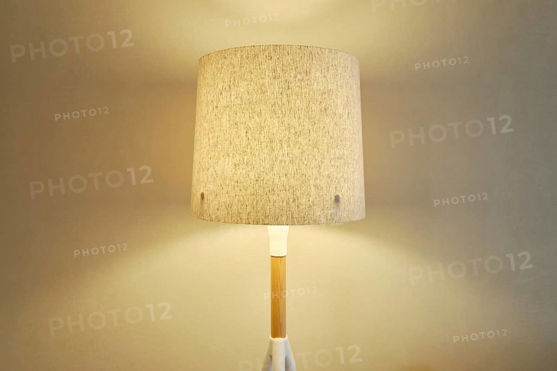 A stylish lamp with a beige fabric shade casting a soft warm light on the wall in the room