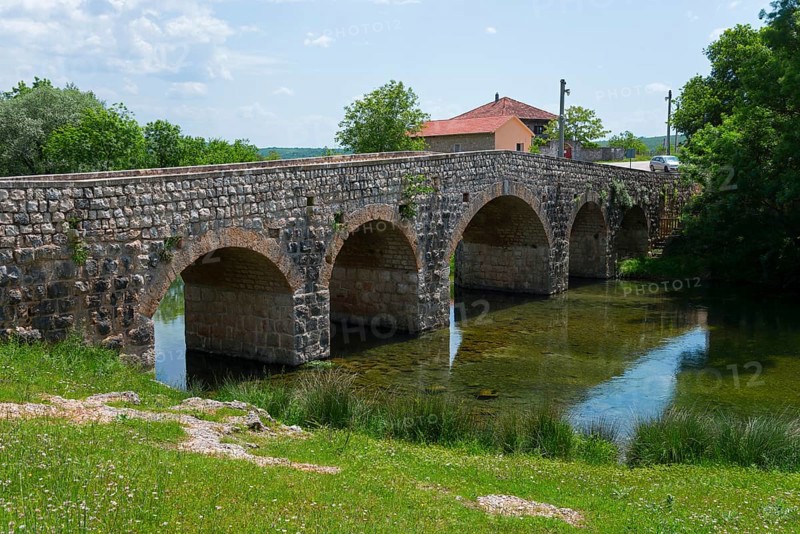Stone bridge over river, flanked by green bank and small building, Bridge over the river Zrmanja, Žegar, Zegar, Zadar, Croatia