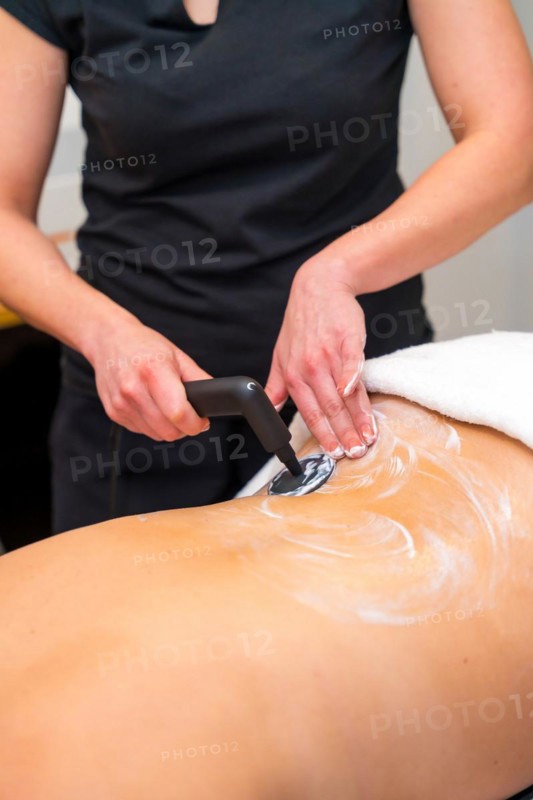 Vertical close-up photo of an unrecognizable massage therapist using the INDIBA machine to relieve back pain in a woman