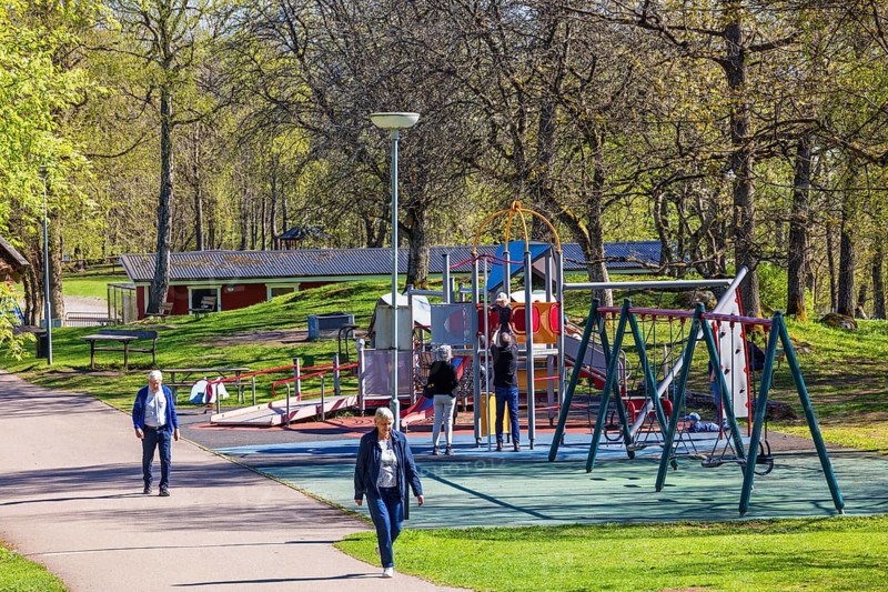 Playground in a public park with children playing and people walking on a footpath at springtime, Mösseberg, Falköping, Sweden
