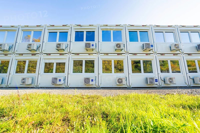 Several white containers with windows and air conditioning units stand on a green meadow, Beermiß refugee accommodation centre, Calmbach, Black Forest, Germany