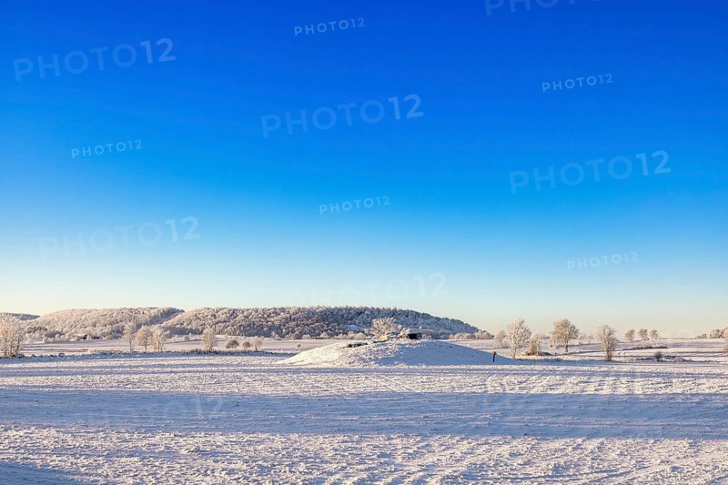 Winter landscape with snow and frost in the countryside with a Passage grave on a hill and a table mountain Ålleberg that is part of the Swedish Unesco geopark Falköping, Karleby, Sweden