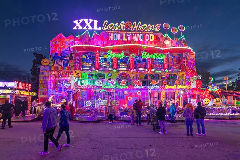 Colourfully illuminated fun house at a funfair at night with numerous visitors, Cannstatter Wasen, folk festival, Bad Cannstatt, Stuttgart, Baden-Württemberg, Germany