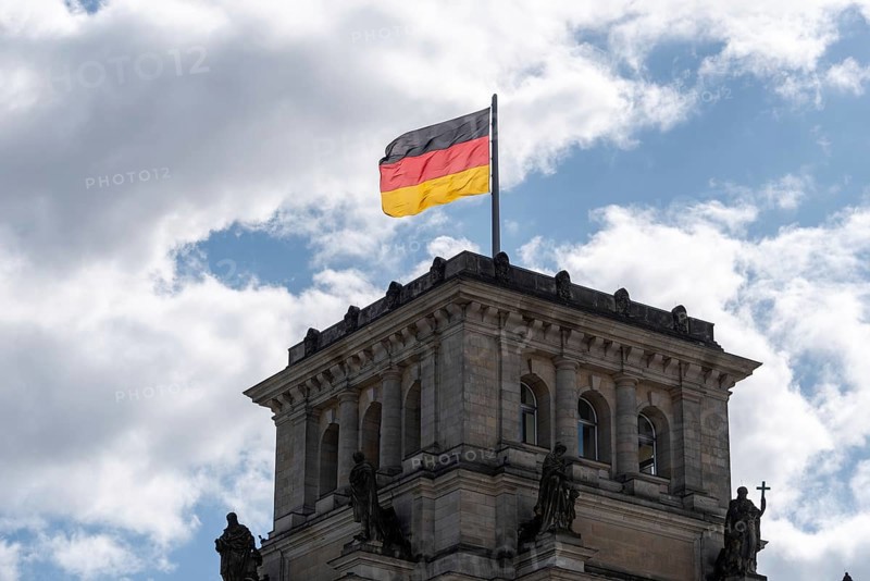 A German flag flies over a building tower of the Reichstag against a cloudy sky, Berlin, Germany