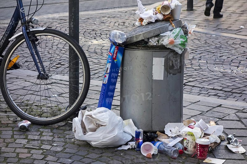 Overfull rubbish bin with trash around and garbage piled on top in city street