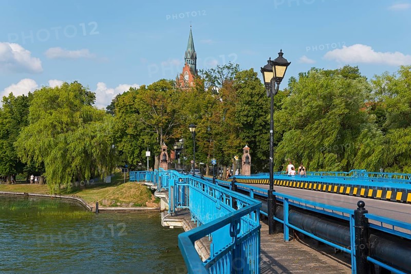 Blue bridge against a lush green backdrop with church tower and lanterns in sunny weather, historic bridge, Elk, Elk, Lyck, Jezioro Elckie, Warmia-Masuria, Poland