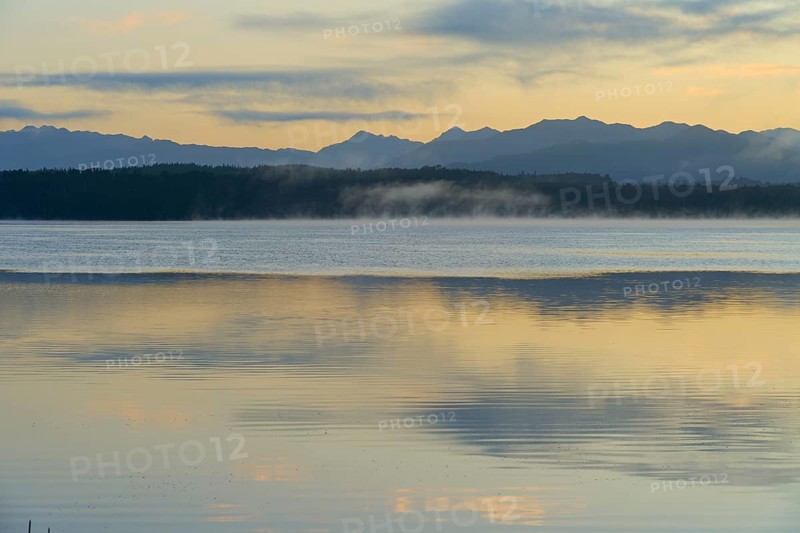 Calm waters with a mountain backdrop under a pastel-coloured sky, Lake Mahinapua, Ruatapu, South Island, New Zealand