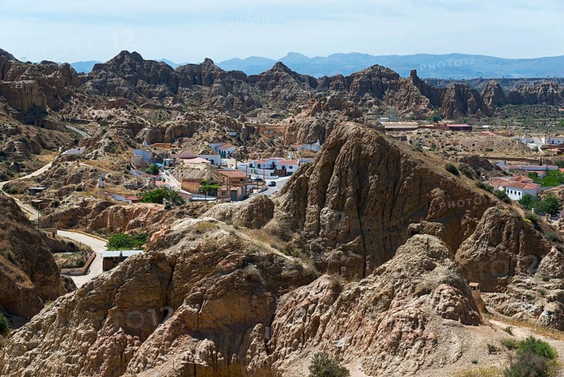 A small village nestled in a rocky, rugged landscape under a sunny sky, view from the Mirador del Cerro de la Bala, cave dwellings, cave district, Troglodytos, Barrio de Cuevas, Guadix, Granada province, Andalusia, Spain