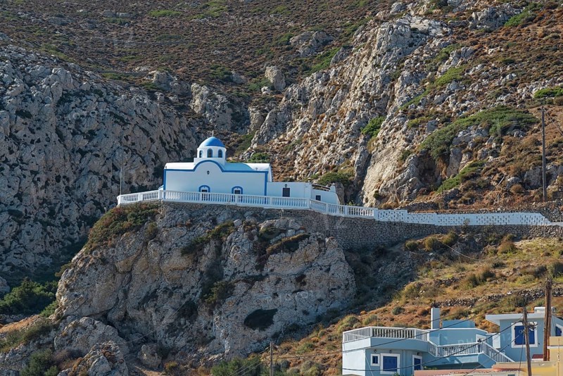 White chapel of Agios Spiridonas with blue roof on a stony rock surrounded by mountains, Menetes, Karpathos, Greece