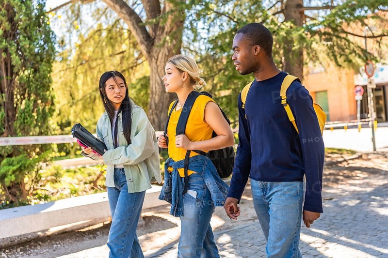 Side view of three multi-ethnic friends walking out the university campus