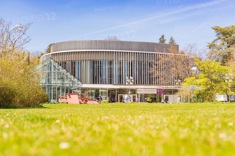 Civic hall Sindelfingen, A modern, round building with a glass façade. Surrounded by green lawns and trees, under a clear blue sky, Sindelfingen, Germany