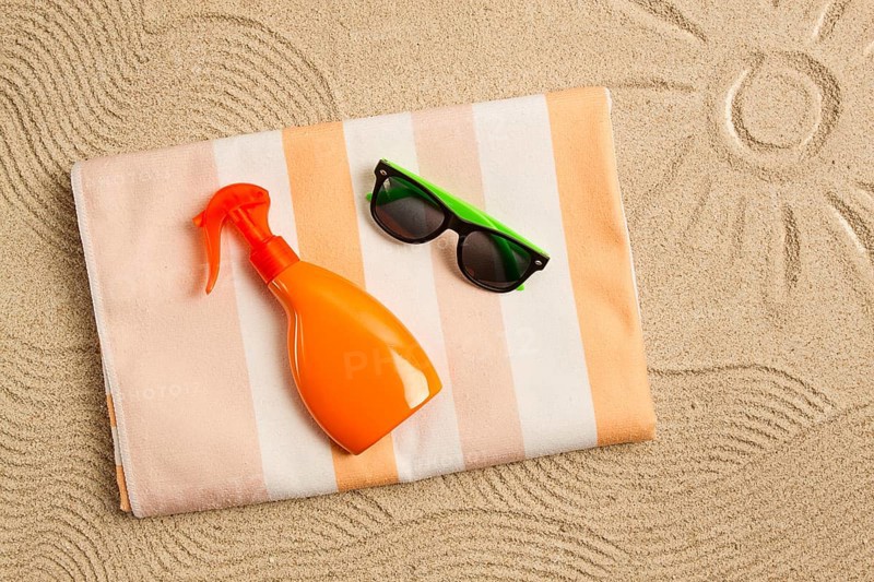 Drawing on the sand, sun and waves, sunglasses, with an orange bottle, beach towel, sun spray, on the sand, top view, no people