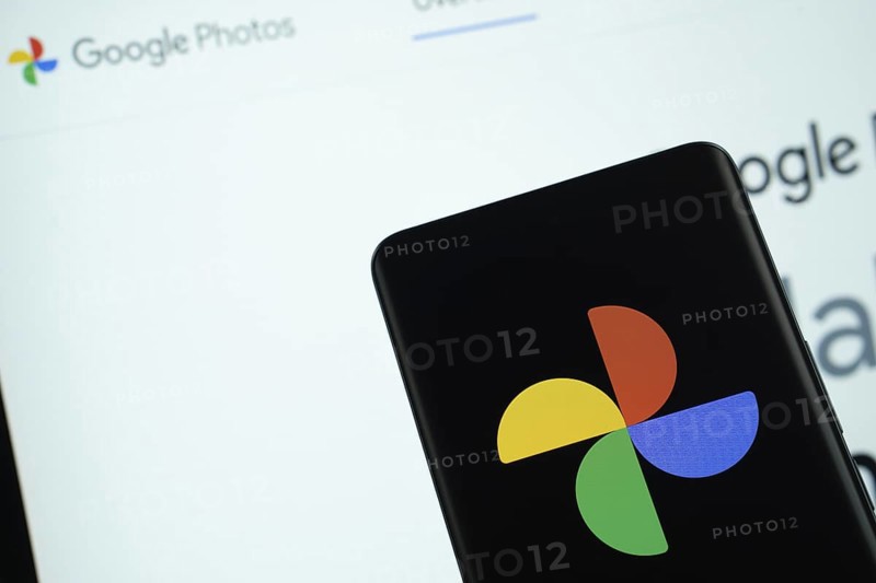 The logo of the google photos is displayed on a smartphone screen, and the website google photos is visible on a computer screen in the background