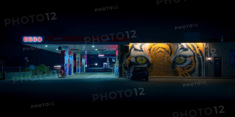 View of a petrol station with a parked car in front of a painted facade at night, Nienburg, Lower Saxony, Germany