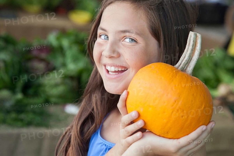 Happy young blue eyed girl holding a fresh pumpkin at the farmers market