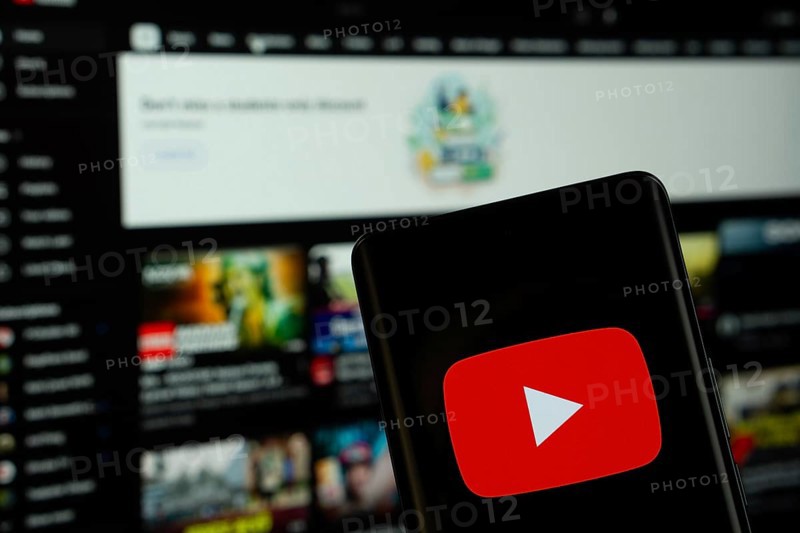 Dhaka, Bangladesh- 10 July 2025: Youtube logo is displayed on a smartphone screen, with the website visible on a computer screen in the background