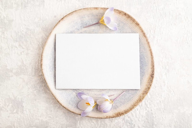 White paper invitation card, mockup with crocus flowers on ceramic plate and gray concrete background. Blank, flat lay, top view, still life, copy space, wedding invitation
