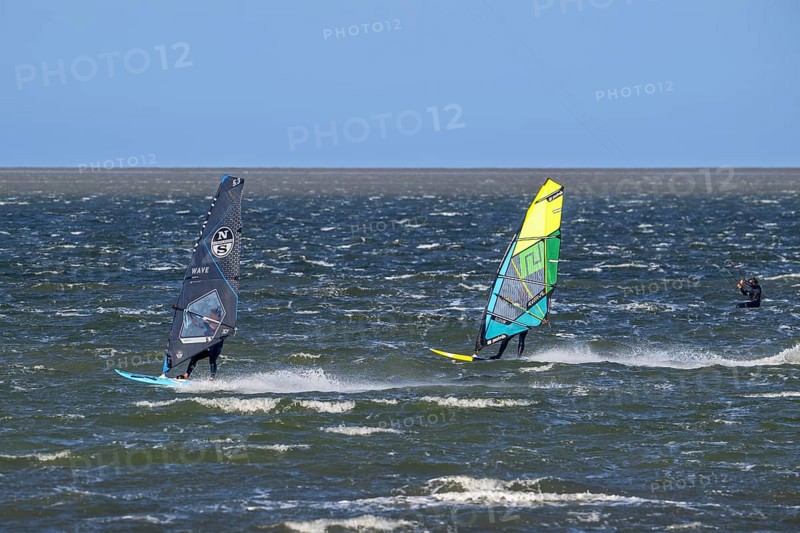 Kiteboarder, kitesurfer and two recreational windsurfers in wetsuits practising classic windsurfing along the North Sea coast in windy weather