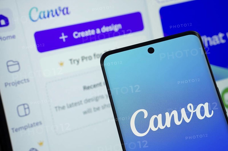Canva logo is displayed on a smartphone screen, with the canva website visible on a computer screen in the background