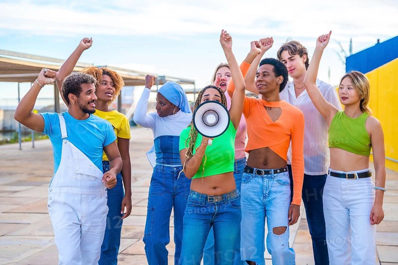 Multicultural and gender diverse young people yelling using a loudspeaker in a protest on an urban space