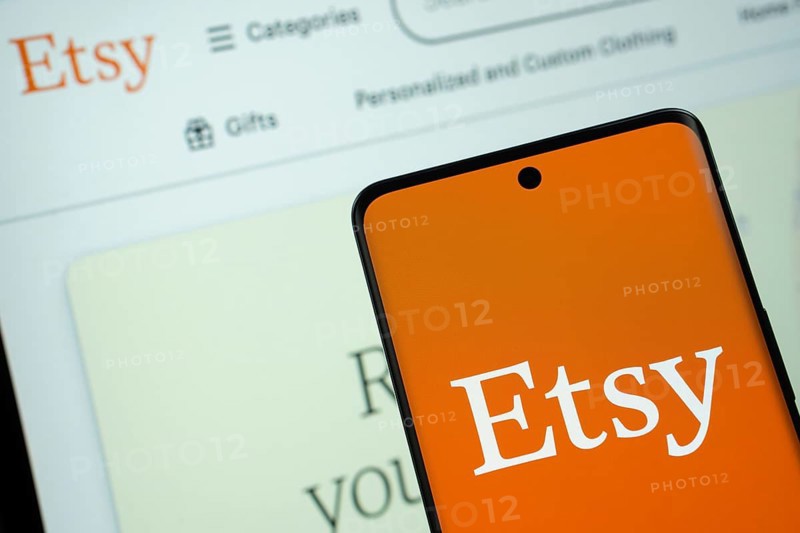 Dhaka, Bangladesh- 08 March 2025: Etsy logo is displayed on a smartphone screen, with the Etsy website visible on a computer screen in the background