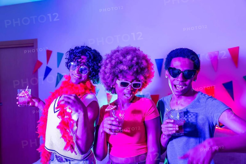 Multiracial friends partying at home at night with colorful neon light illuminating the apartment