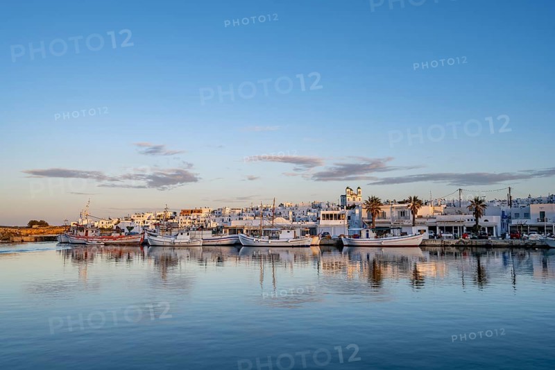 View of Naoussa, Fishing boats in the harbour at sunset, reflected in the sea, White Cycladic houses and church Agios Faneromeni, Naoussa, Paros, Cyclades, Greece