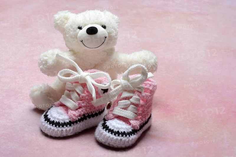 Pink baby shoes with teddy bear, pink background