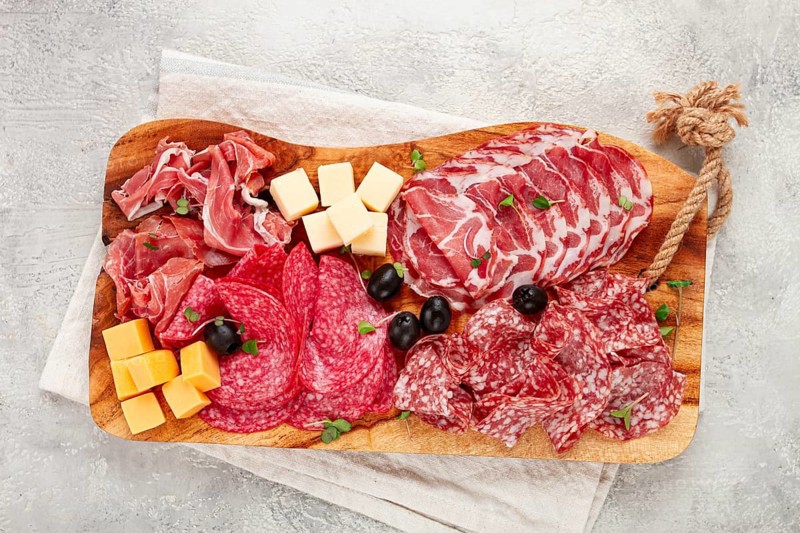 Assorted, sliced meat appetizer, prosciutto, salami and ham, with cheese and olives, on a wooden board, breakfast, top view, close-up, no people