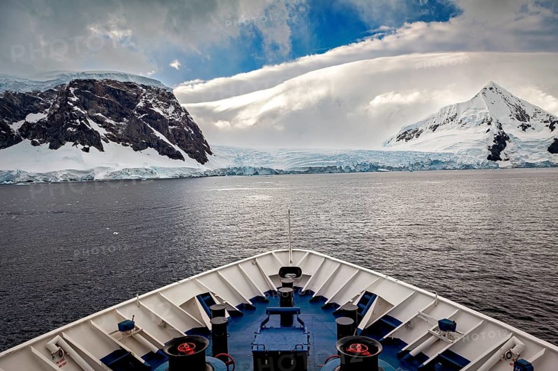 The view from the bow of a ship shows majestic mountains under a dramatic sky, cruise ship underway in the Southern Ocean in Antarctica