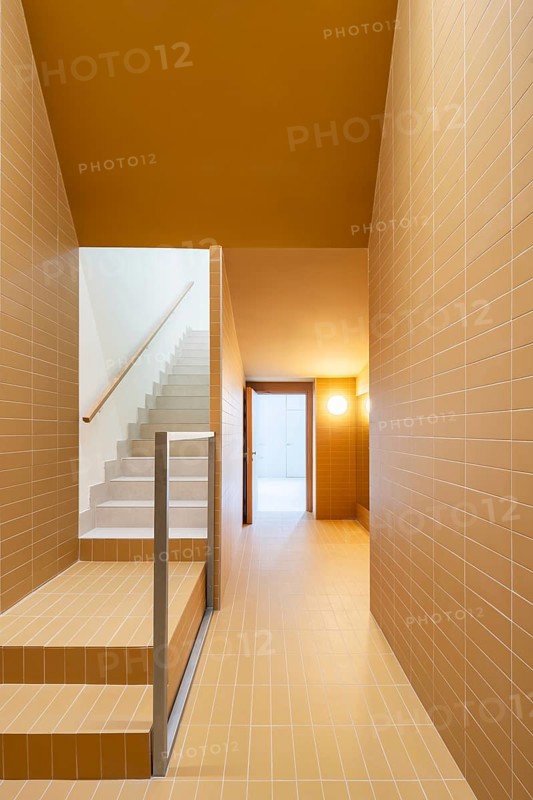 A modern staircase and hallway showcase sustainable architecture with vibrant orange and cream colors tiles, promoting a low-emission design and passive house efficiency standards