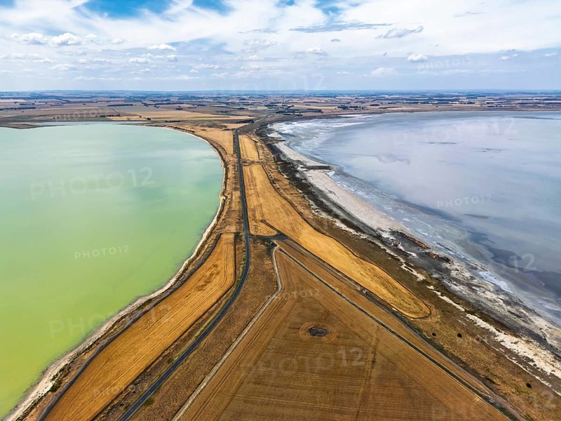 Aerial photo contrasting vibrant green and gray lakes divided by roads and golden fields in Victoria, Australia. Cloudy sky adds depth to this serene landscape, highlighting nature beauty