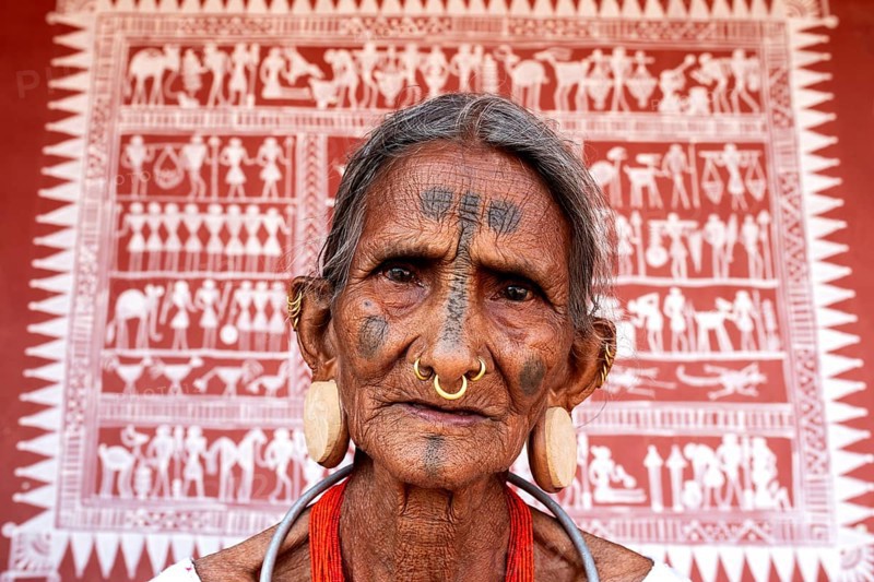 Portrait of a woman from the Lanjia Saora tribe (Odisha, India) . Behind her, a Lanjia Saora traditional mural painting