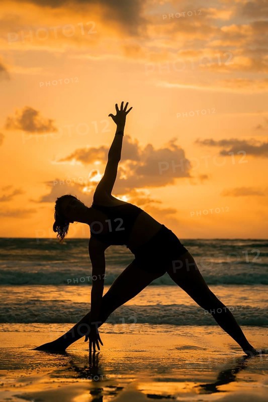 A serene silhouette of a woman practicing yoga on a beach during sunset in Tulum, Mexico. The warm glow of the sun reflects off the sand, creating a peaceful atmosphere